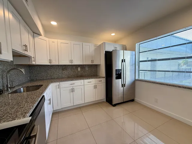 a kitchen with stainless steel appliances granite countertop a refrigerator a sink and white cabinets