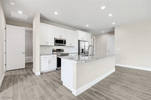 a large white kitchen with wooden floor and stainless steel appliances