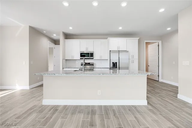 a view of kitchen with stainless steel appliances granite countertop a stove a sink a refrigerator and white cabinets with wooden floor