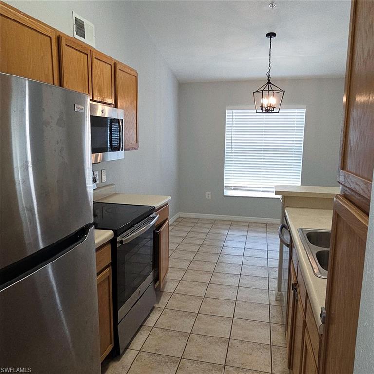7940 Preserve Circle, Unit 935 Naples, FL 34119 - Photo 1 of 7 Kitchen featuring stainless steel appliances, brown cabinetry, light countertops, hanging light fixtures, and light tile patterned flooring