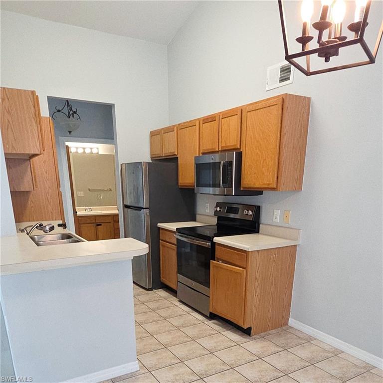 7940 Preserve Circle, Unit 935 Naples, FL 34119 - Photo 4 of 7 Kitchen featuring stainless steel appliances, light countertops, light tile patterned floors, and a chandelier