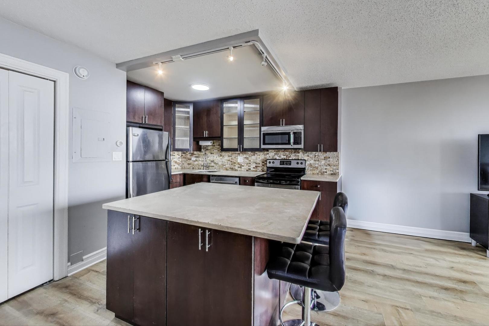 2930 North Sheridan Road, Unit 2111 Chicago, IL 60657 - Photo 9 of 31 a kitchen with kitchen island wooden cabinets a refrigerator stove a sink and a oven