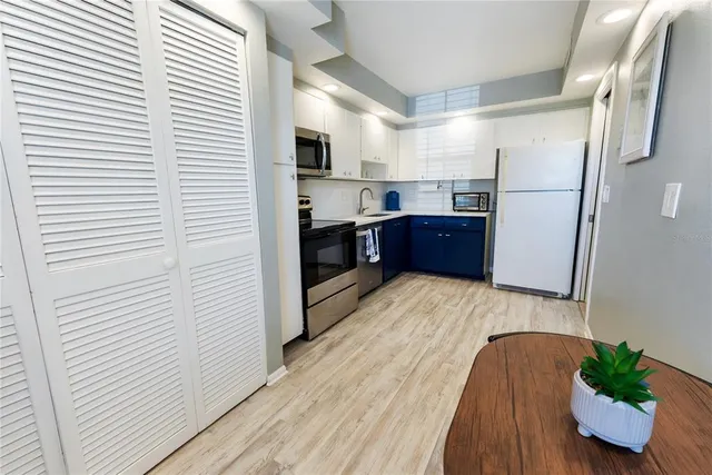 a kitchen with stainless steel appliances granite countertop a refrigerator a sink dishwasher a stove and white countertops with wooden floor