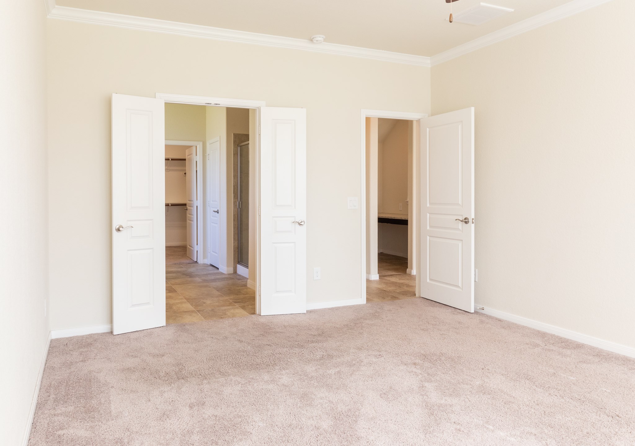 10 Log House Court Tomball, TX 77375 - Photo 25 of 50 This photo shows a bright, carpeted bedroom with neutral walls, featuring double doors leading to a tiled en suite bathroom and a walk-in closet.