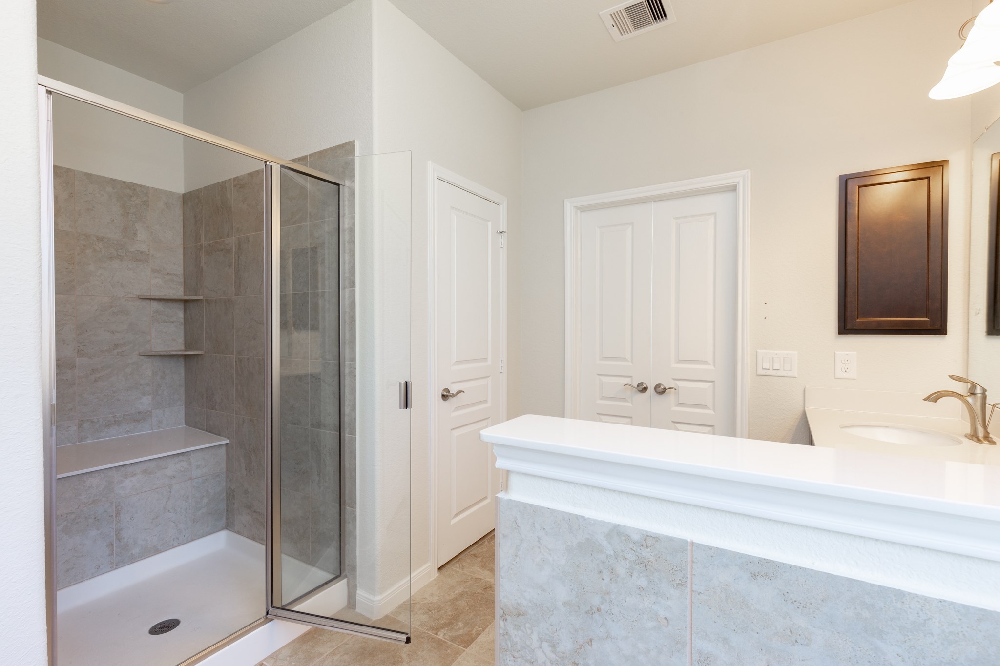 10 Log House Court Tomball, TX 77375 - Photo 33 of 50 This bathroom features a spacious glass-enclosed shower with built-in shelves and a bench. It has a clean, modern design with neutral tiles, a single sink vanity, and ample storage space.