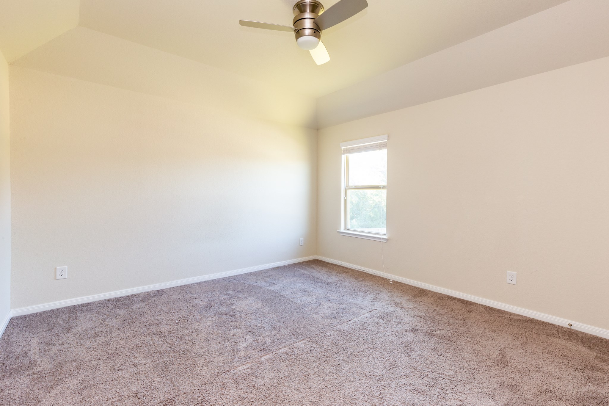 10 Log House Court Tomball, TX 77375 - Photo 38 of 50 This photo shows a bright, empty room with neutral walls and carpet. It features a single window providing natural light and a ceiling fan.