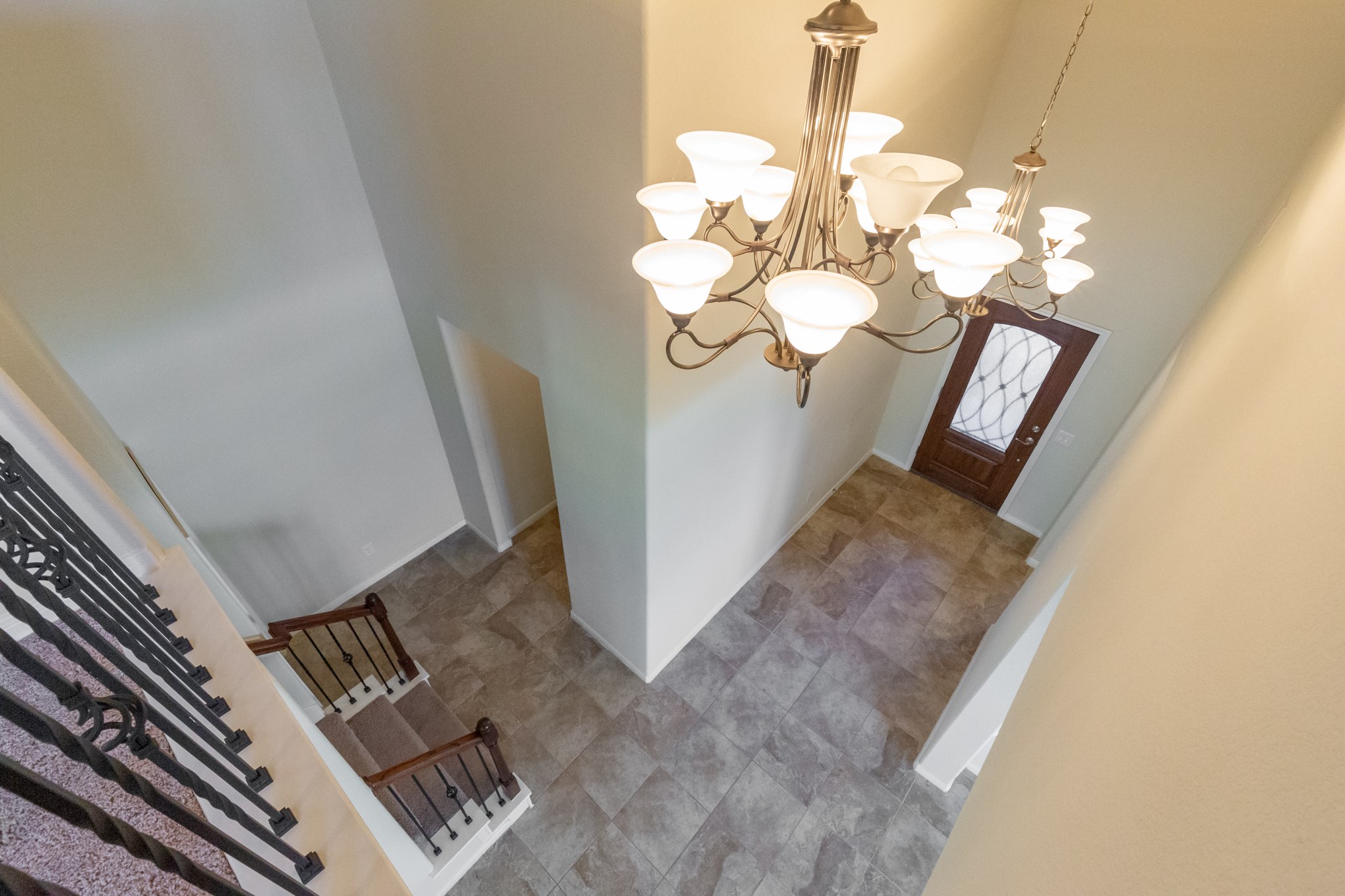 10 Log House Court Tomball, TX 77375 - Photo 4 of 50 This photo showcases a spacious entryway with high ceilings, a stylish chandelier, and a wooden front door with glass detailing. The tiled floor and elegant staircase with wrought iron balusters add a touch of sophistication.