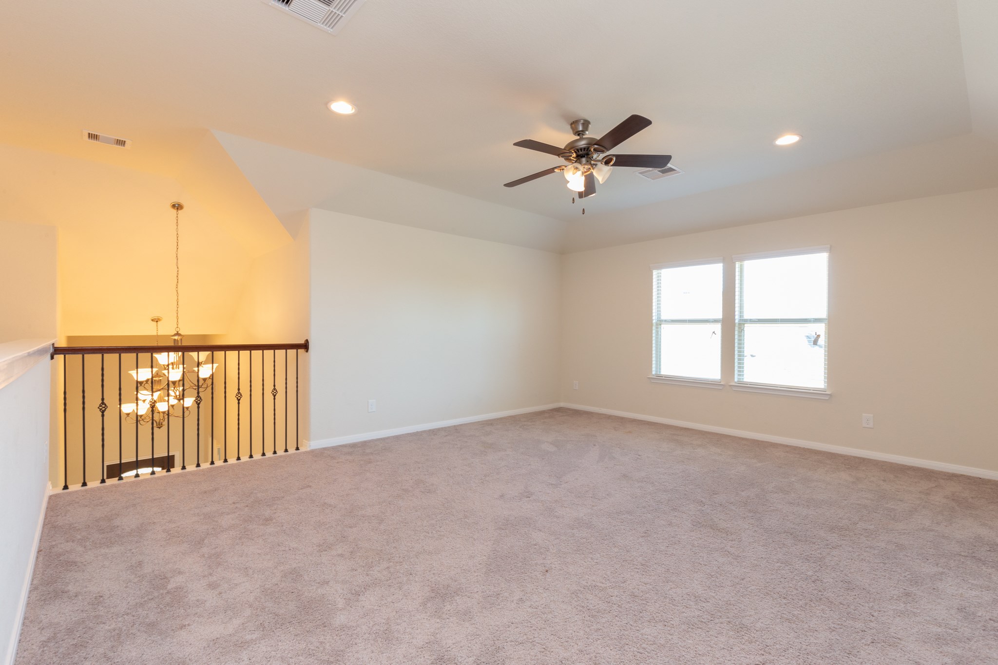 10 Log House Court Tomball, TX 77375 - Photo 44 of 50 This spacious room features plush carpeting, a ceiling fan, and ample natural light from two windows. It overlooks a grand chandelier through a stylish iron railing, offering an elegant touch to the open layout.