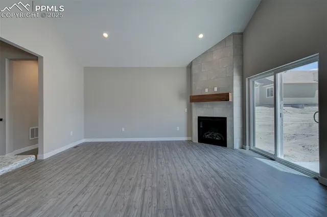 a view of an empty room with wooden floor fireplace and a window