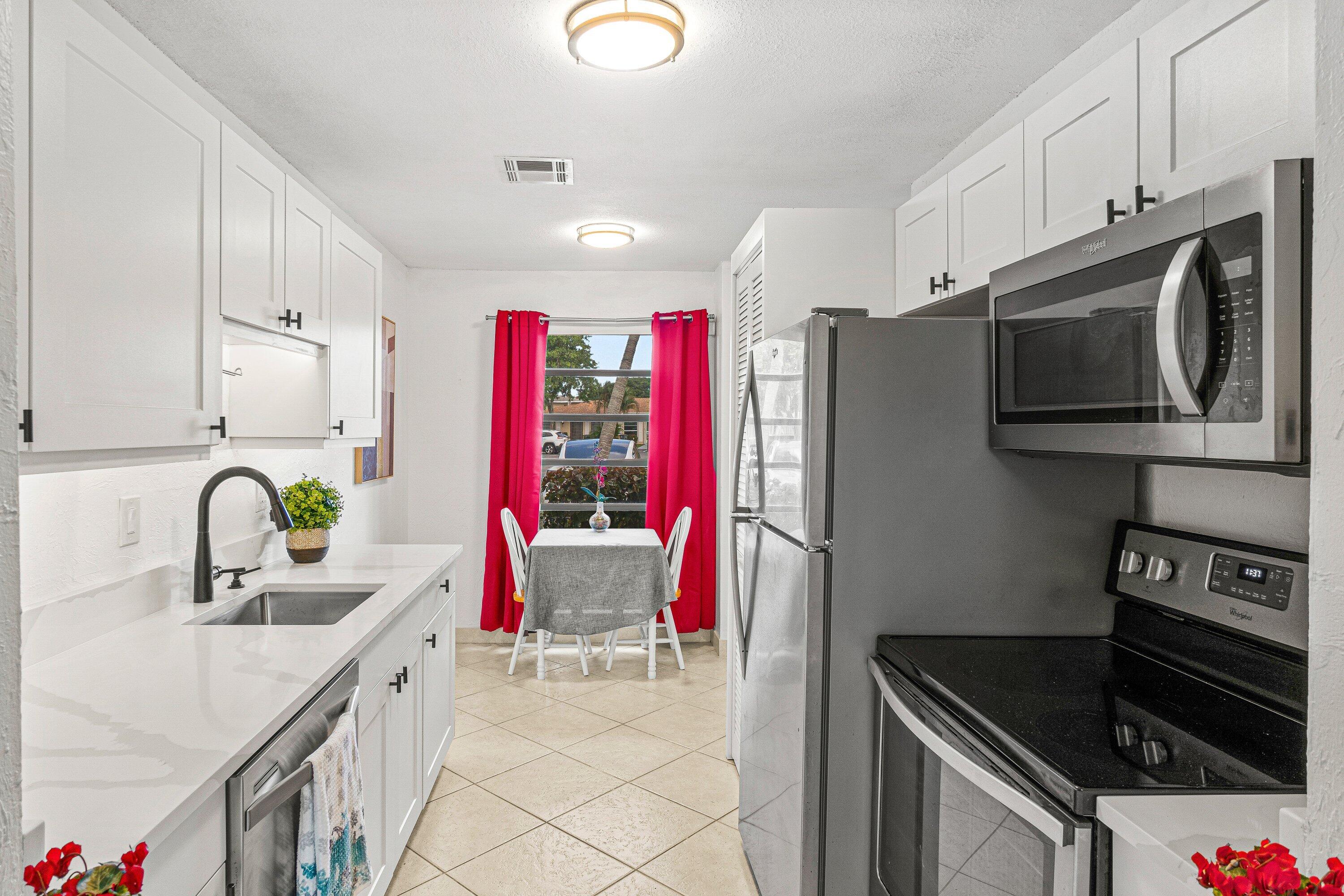 13899 Via Aurora, Unit C Delray Beach, FL 33484 - Photo 2 of 39 a kitchen with stainless steel appliances kitchen island granite countertop a sink dishwasher stove and refrigerator with wooden cabinets