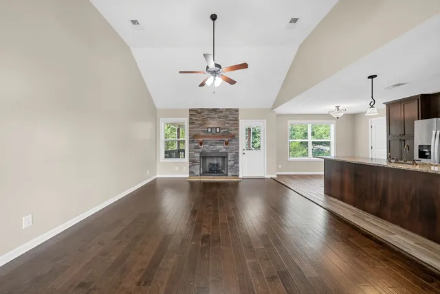 an empty room with wooden floor chandelier fan and windows