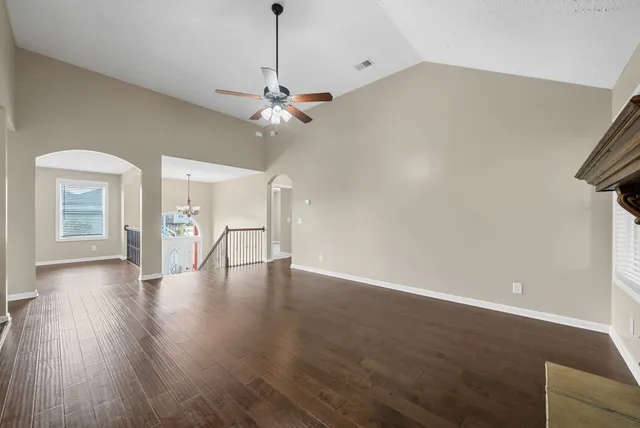 a view of an empty room with wooden floor and a ceiling fan
