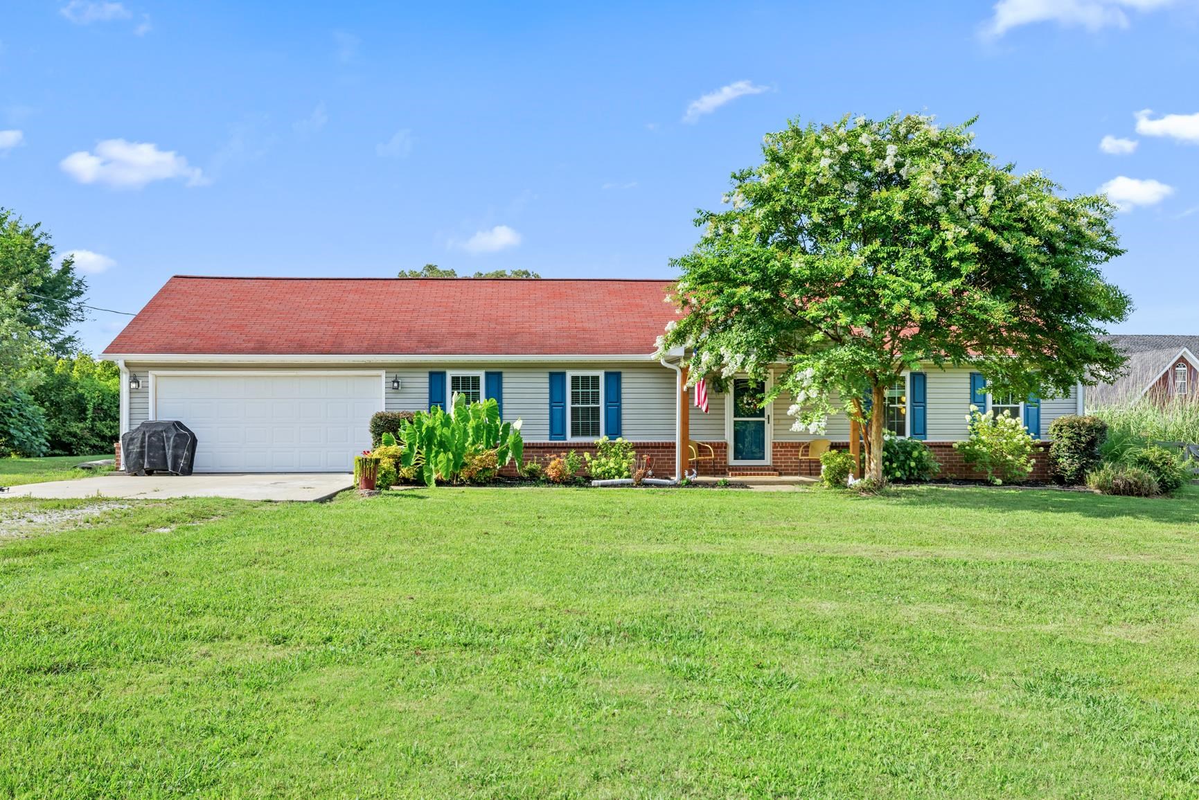 Ranch-style home featuring driveway, an attached garage, a front lawn, and brick siding