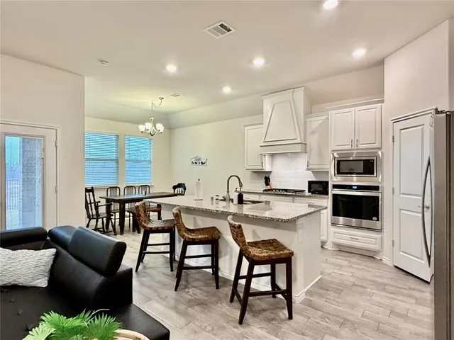 a kitchen with stainless steel appliances kitchen island granite countertop a sink a stove a refrigerator and white cabinets with wooden floor