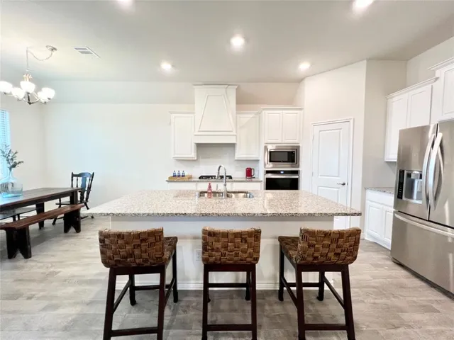 a kitchen with stainless steel appliances granite countertop a dining table chairs refrigerator and microwave