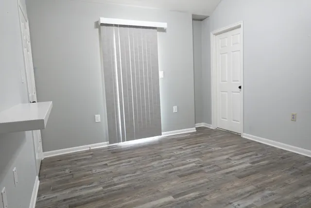 a view of an empty room with wooden floor and a window