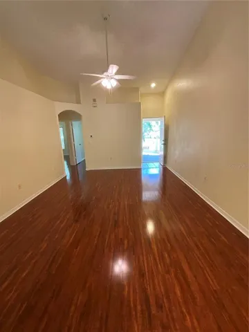 a view of an empty room with wooden floor and a ceiling fan