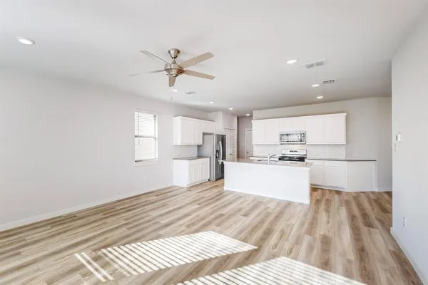 a large white kitchen with kitchen island a stove a refrigerator a sink dishwasher with a dining table and chairs with wooden floor