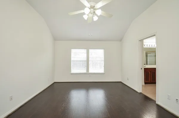 an empty room with wooden floor chandelier fan and windows