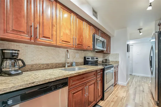 a kitchen with granite countertop wooden cabinets a sink a stove and a refrigerator