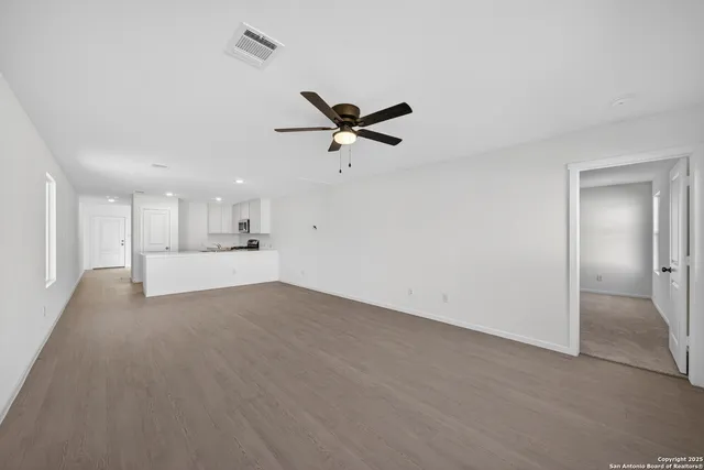 a view of an empty room with a ceiling fan and kitchen view
