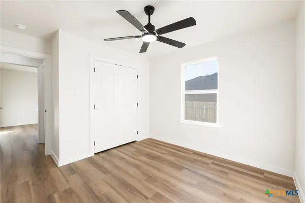 an empty room with wooden floor ceiling fan and windows