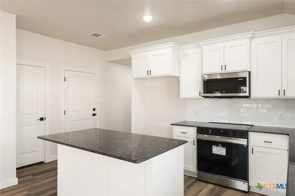 a large kitchen with stainless steel appliances granite countertop a stove a sink and white cabinets
