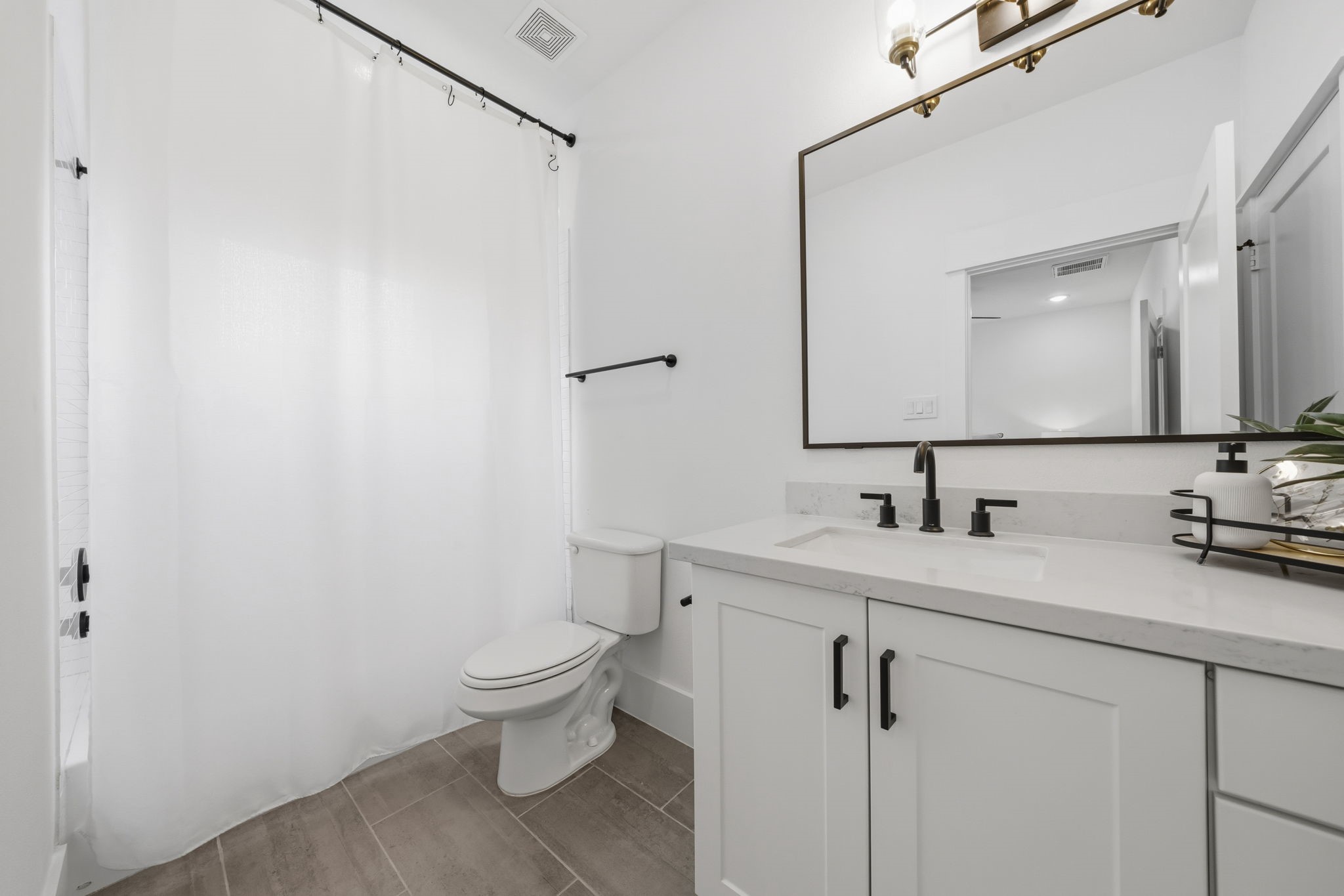 9018 Wellspring Drive Houston, TX 77080 - Photo 17 of 25 The spa-like primary bath boasts a dual-sink vanity with clean white cabinetry and sleek black hardware. The neutral tile flooring and contemporary lighting fixtures complete this refreshed, modern space.