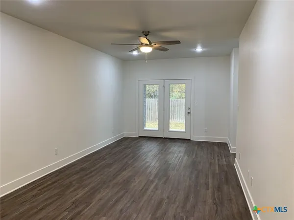 a view of an empty room with wooden floor and a fan
