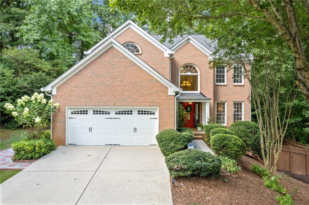 a view of a brick house with large windows and a yard with plants and large trees