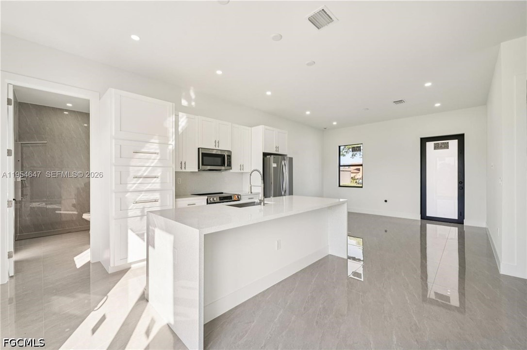 4402 East 19th Street Lehigh Acres, FL 33972 - Photo 5 of 27 a kitchen with stainless steel appliances a refrigerator a sink a stove and white cabinets with wooden floor