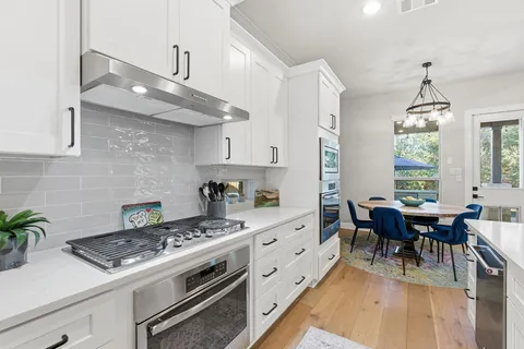 a kitchen with stainless steel appliances granite countertop a stove a sink dishwasher and white cabinets with wooden floor