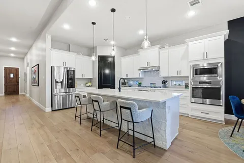 a kitchen with stainless steel appliances granite countertop a refrigerator a stove top oven a sink dishwasher and a dining table with wooden floor