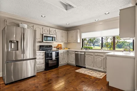 a kitchen with granite countertop a refrigerator a sink dishwasher a stove and a microwave oven with cabinets