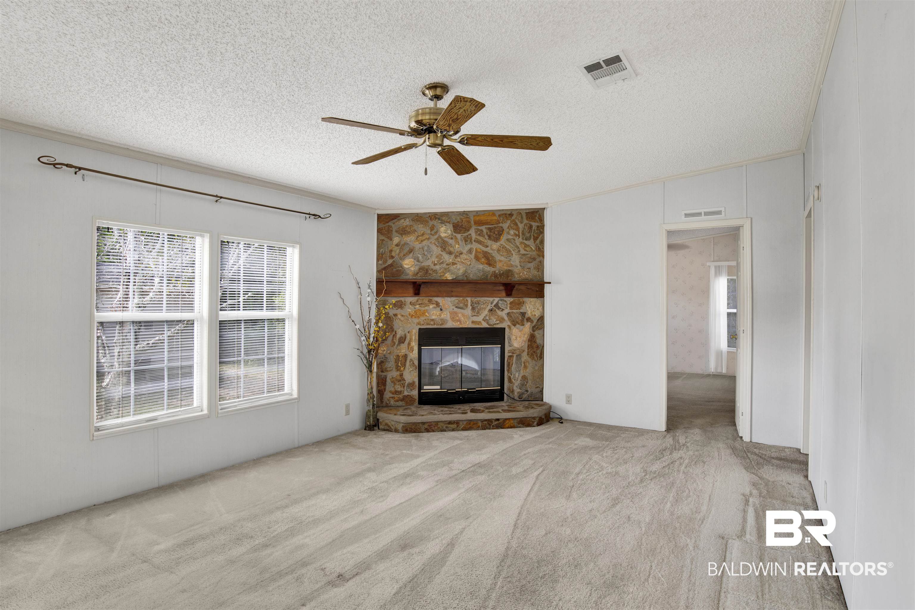 1216 Ridgewood Drive Lillian, AL 36549 - Photo 5 of 29 Unfurnished living room featuring light colored carpet, crown molding, a stone fireplace, a textured ceiling, and ceiling fan