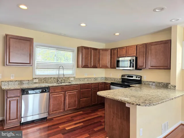 a kitchen with granite countertop wooden cabinets a sink dishwasher a stove and a refrigerator