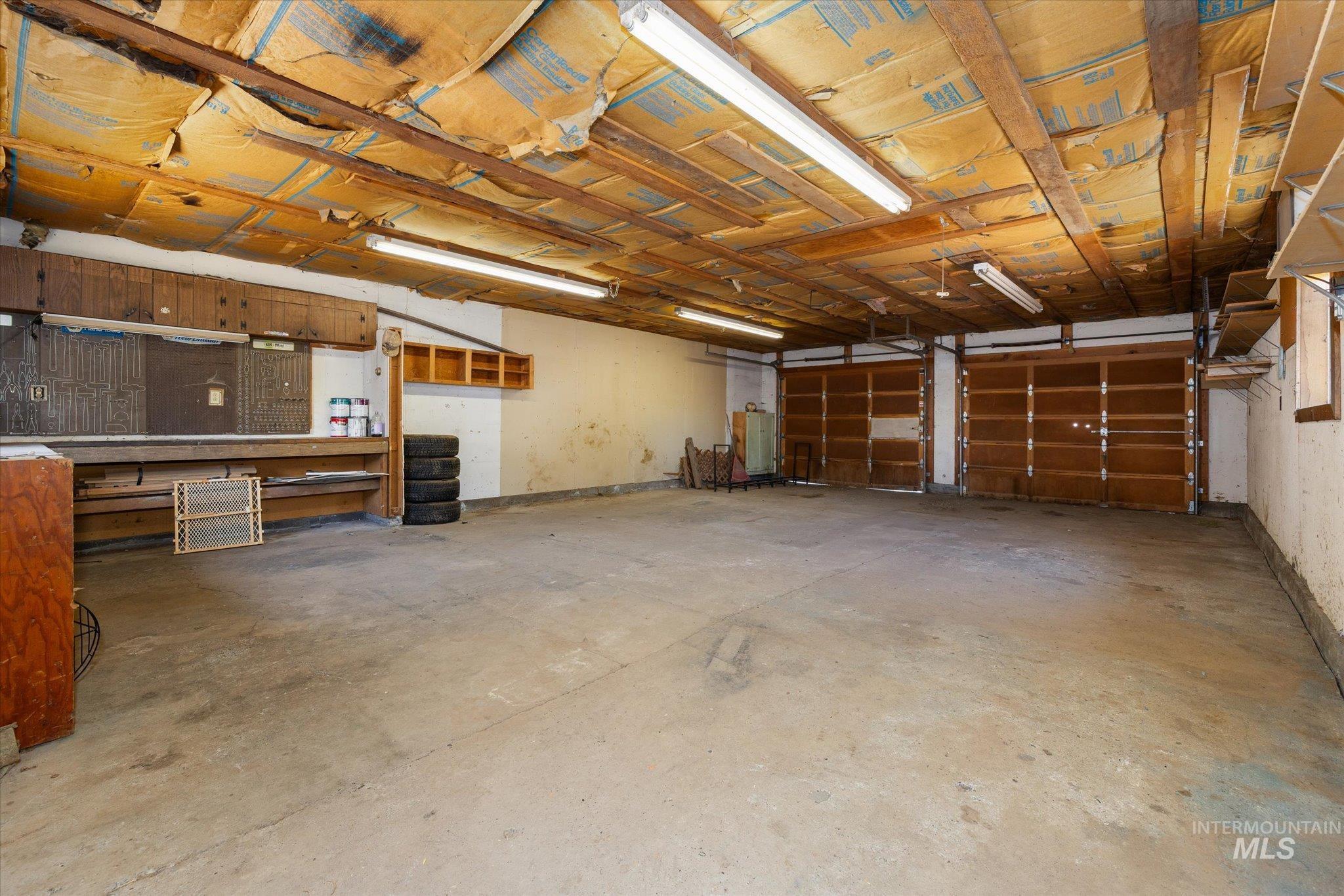 918 West 3rd Street Weiser, ID 83672 - Photo 34 of 36 Two-car garage featuring exposed wood beam ceiling, concrete flooring, fluorescent lighting, and built-in shelving