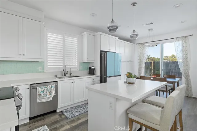 a open kitchen with stainless steel appliances granite countertop a stove a refrigerator a sink dishwasher a dining table and chairs with wooden floor