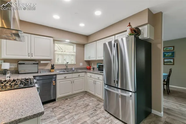 a kitchen with stainless steel appliances granite countertop a refrigerator a sink a stove and white cabinets