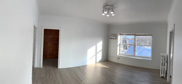 a view of an empty room with a window and wooden floor