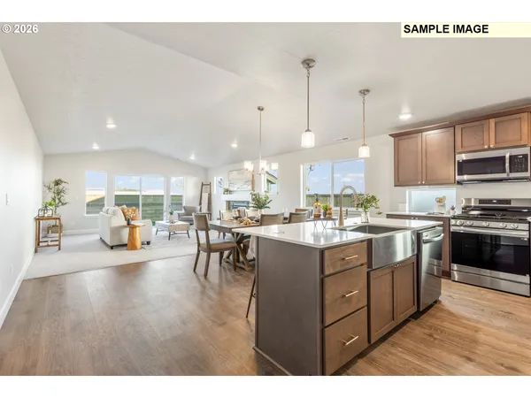 a kitchen with stainless steel appliances granite countertop a refrigerator a sink dishwasher a stove and a dining table with wooden floor