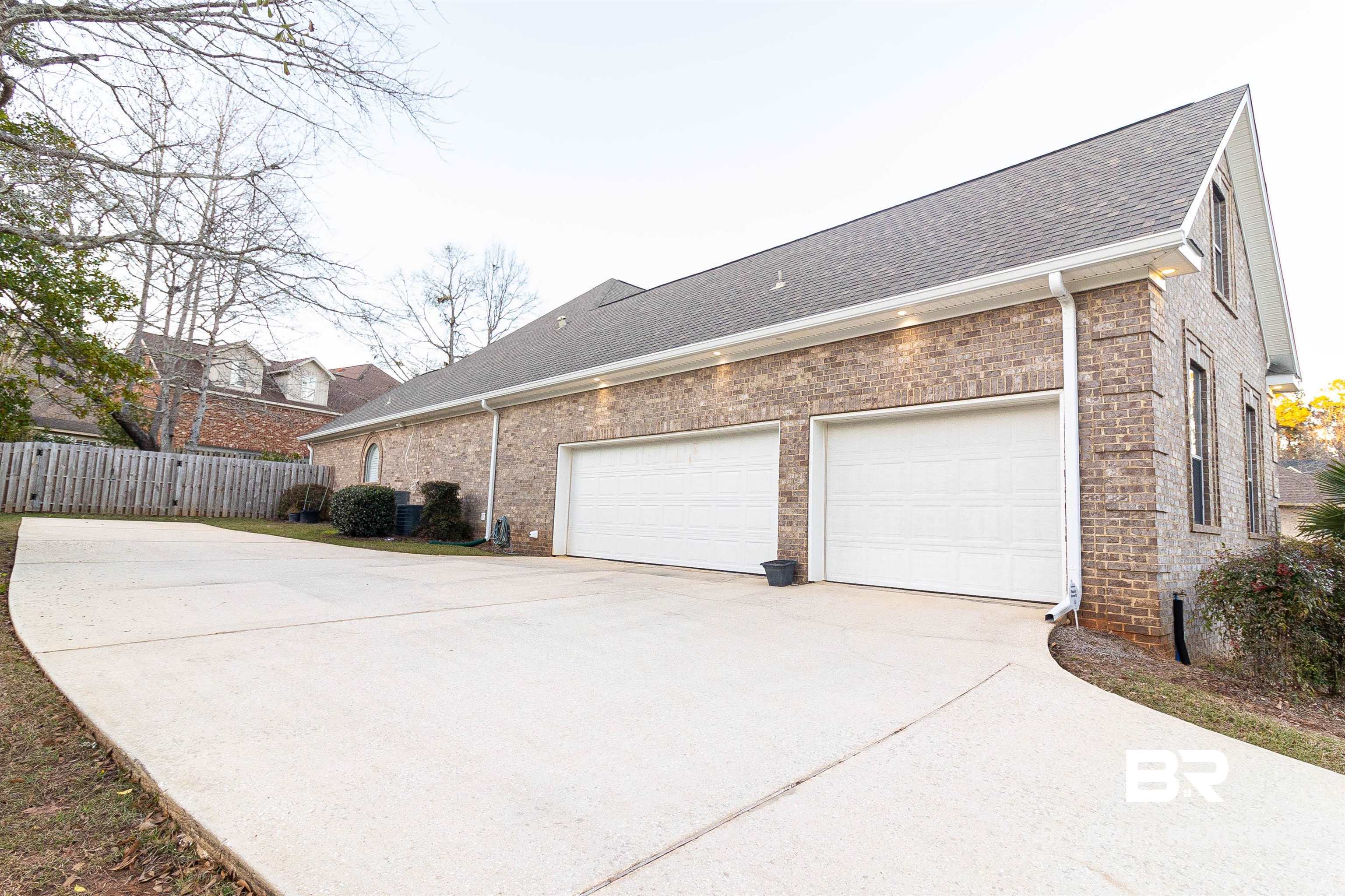 7211 Rushing Water Court Daphne, AL 36527 - Photo 5 of 51 View of property exterior featuring driveway, roof with shingles, an attached garage, fence, and brick siding