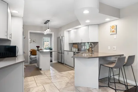 a kitchen with stainless steel appliances kitchen island granite countertop a refrigerator a stove a sink and a dining table with white cabinets