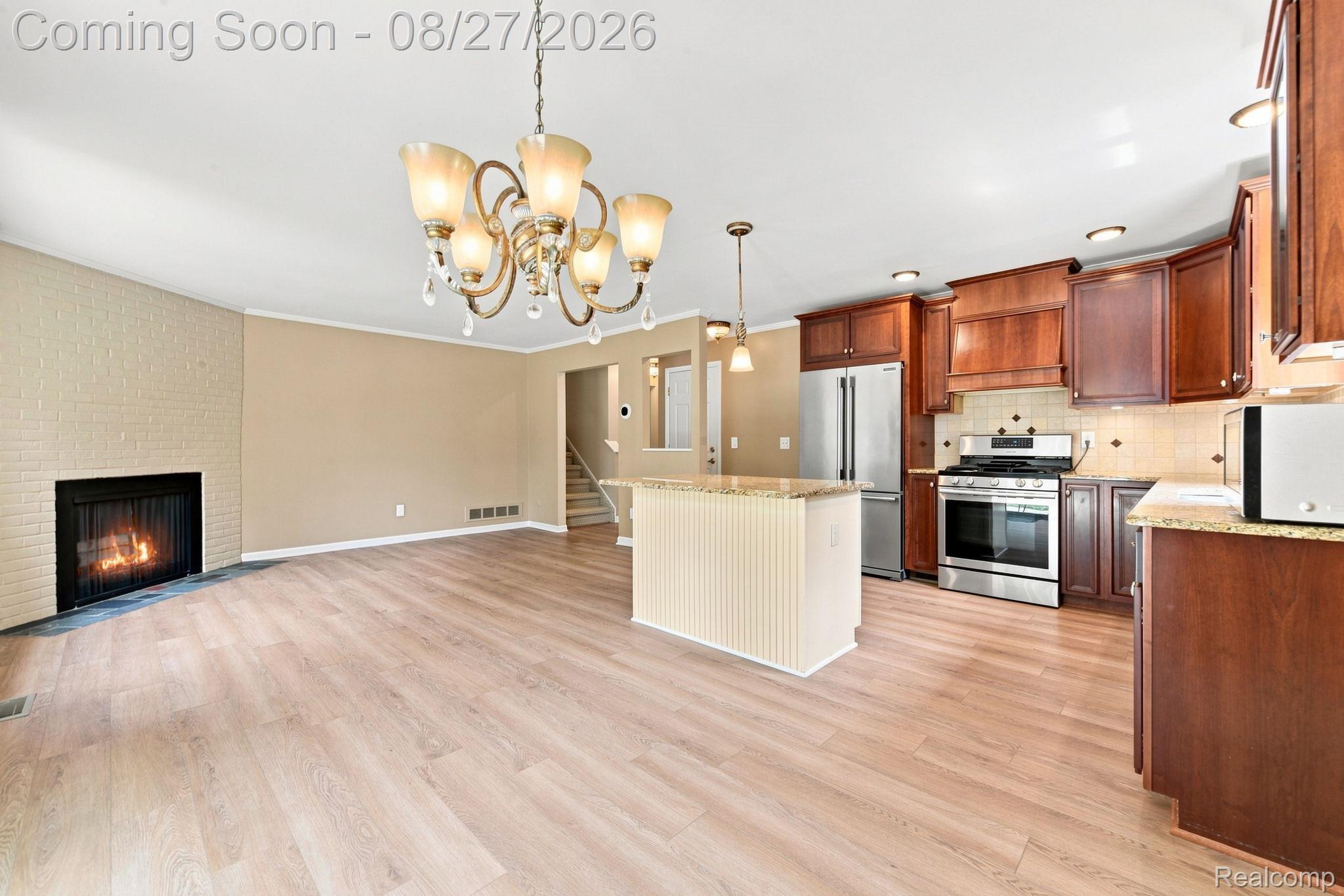 42120 Ridge Road West Novi, MI 48375 - Photo 19 of 32 Open-concept living area with light wood-finish flooring, a brick-surround fireplace, and a decorative chandelier