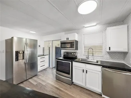 a kitchen with stainless steel appliances a sink dishwasher a refrigerator and white cabinets with wooden floor