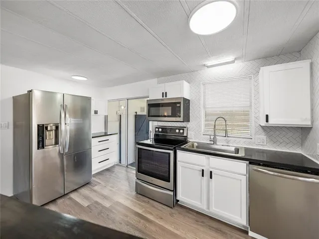 a kitchen with stainless steel appliances a sink dishwasher a refrigerator and white cabinets with wooden floor