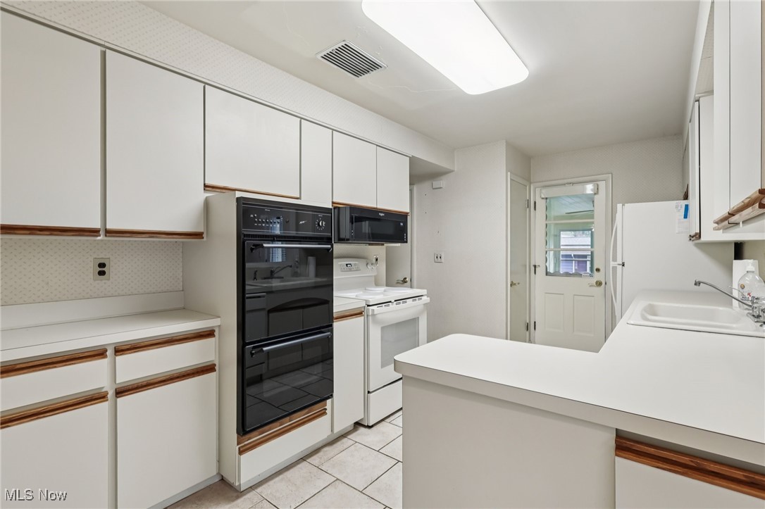 33300 South Woodland Road Cleveland, OH 44124 - Photo 23 of 50 Kitchen with white cabinets, black appliances, light countertops, and a peninsula