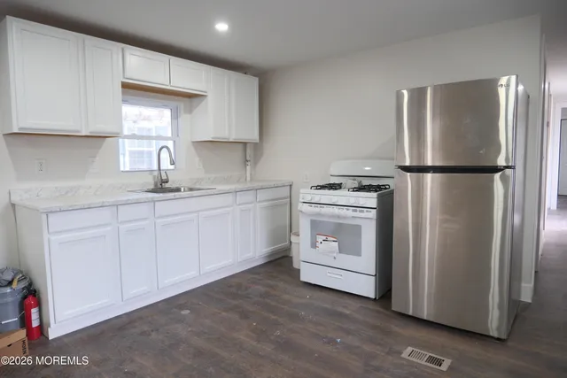 a kitchen with a white refrigerator oven a sink dishwasher and white cabinets with wooden floor