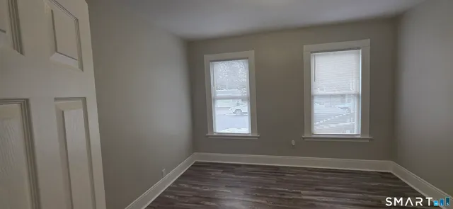 a view of an empty room with wooden floor and window