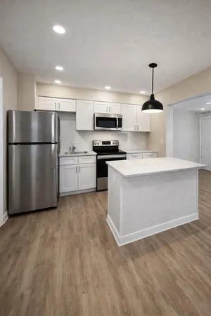 a kitchen with stainless steel appliances granite countertop a stove a refrigerator a sink a microwave oven with white cabinets and wooden floor